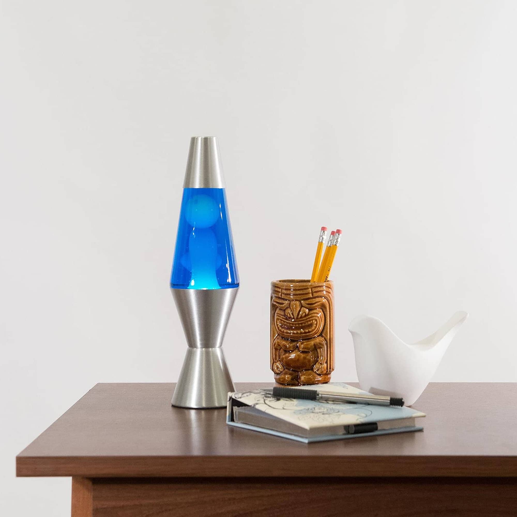 11.5” LAVA® Lamp – White/Blue/Silver on table with notebook and tiki mug